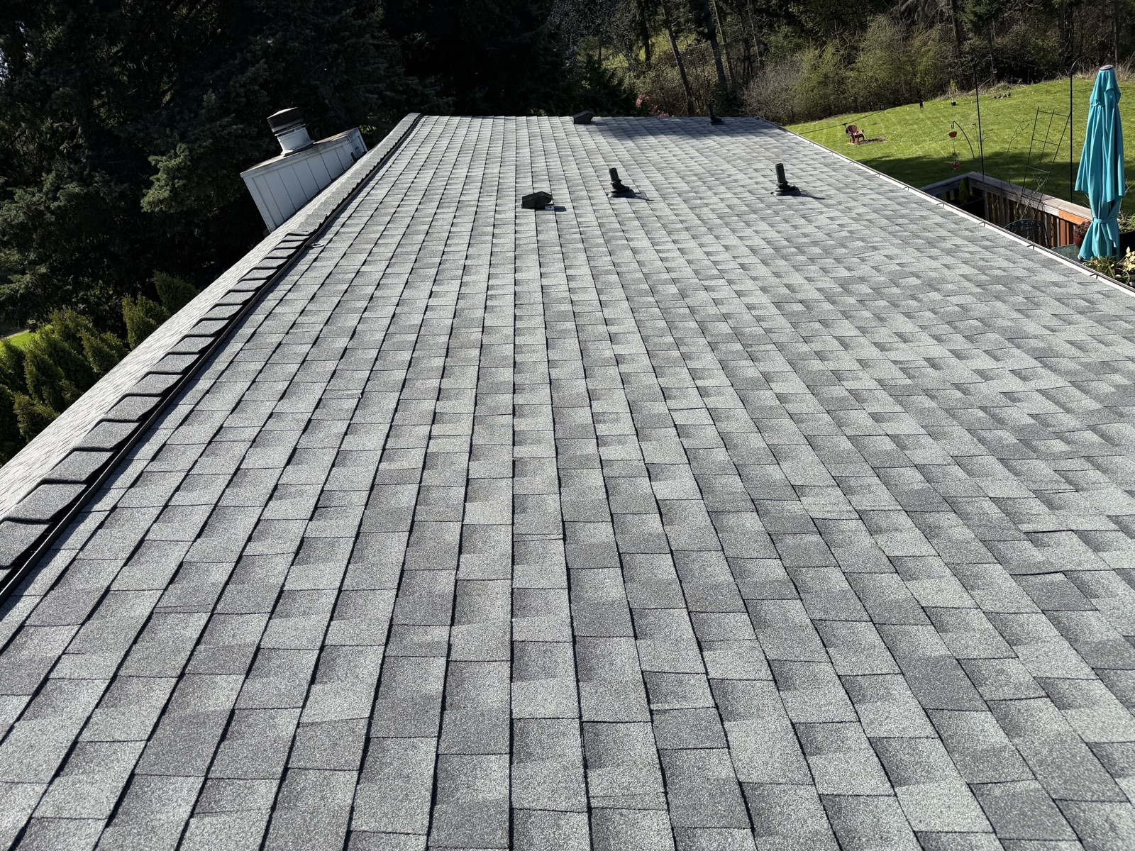 The same slope with new gray architectural shingles, new pipe boots, a new ridge cap and the same white chimney chase