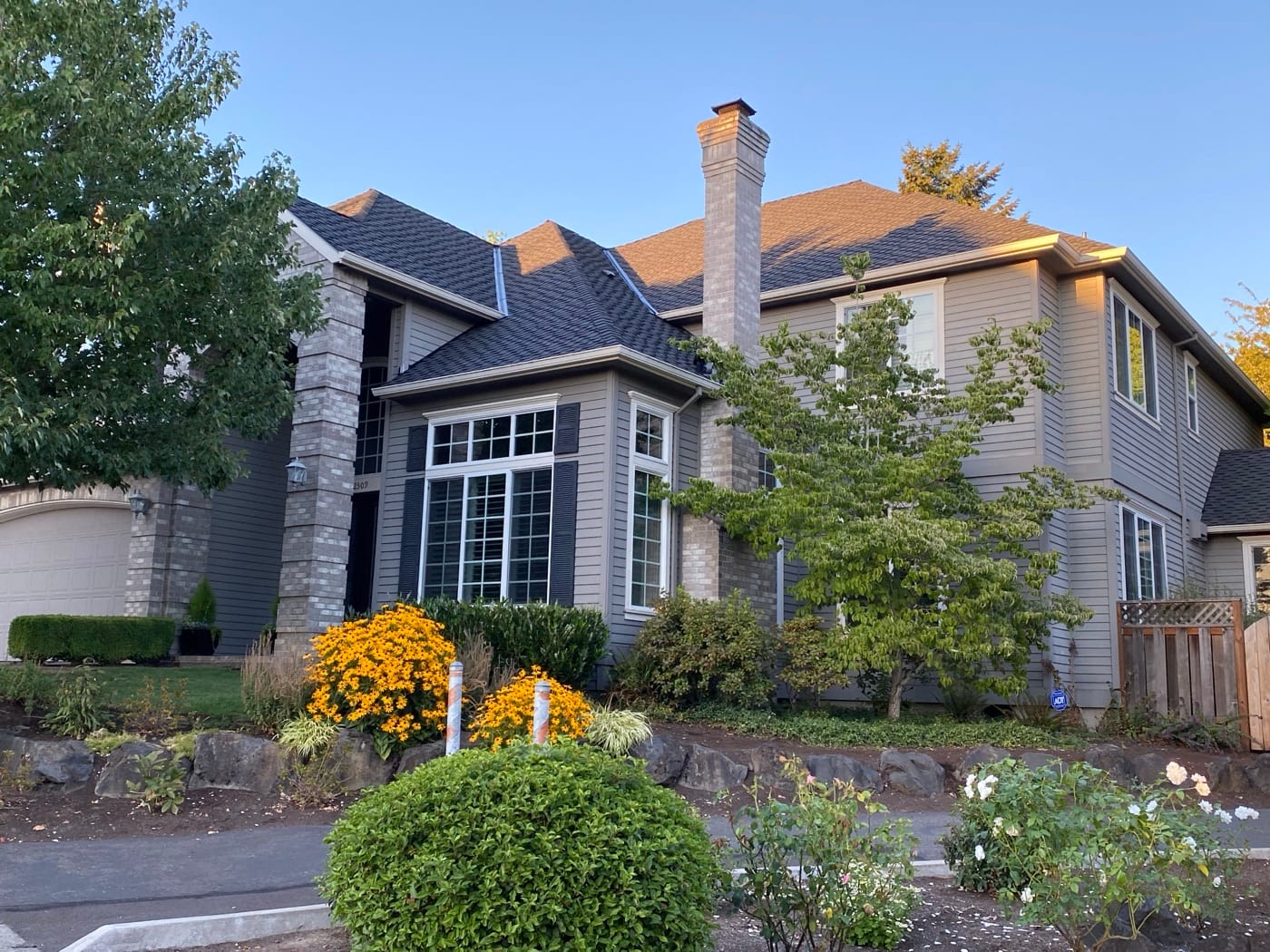 Two-story home with a new dark comp roof at golden hour, flower beds in front